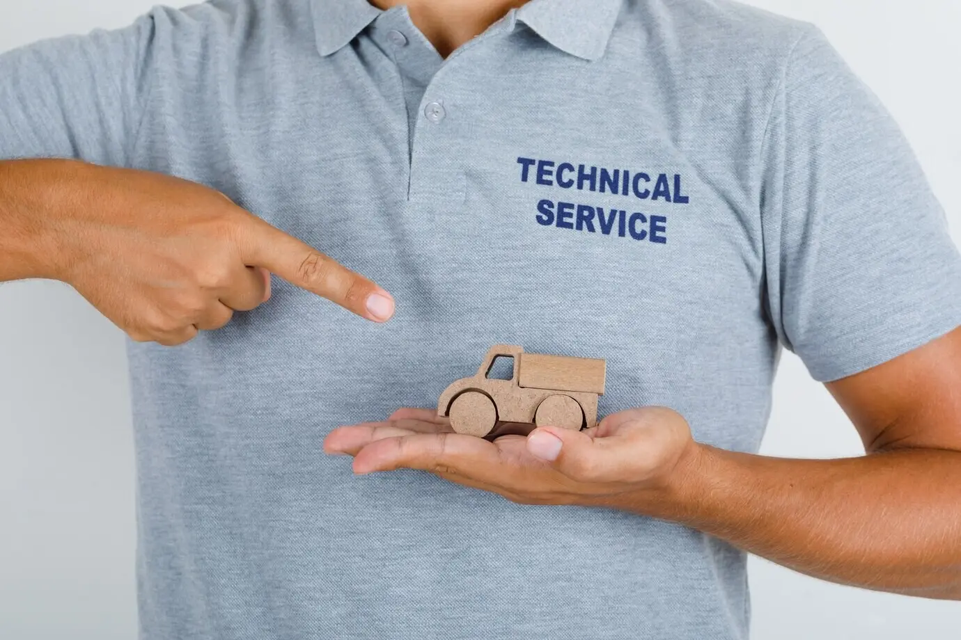 Technischer Servicemitarbeiter zeigt ein Spielzeugauto aus Holz in grauem T-Shirt.