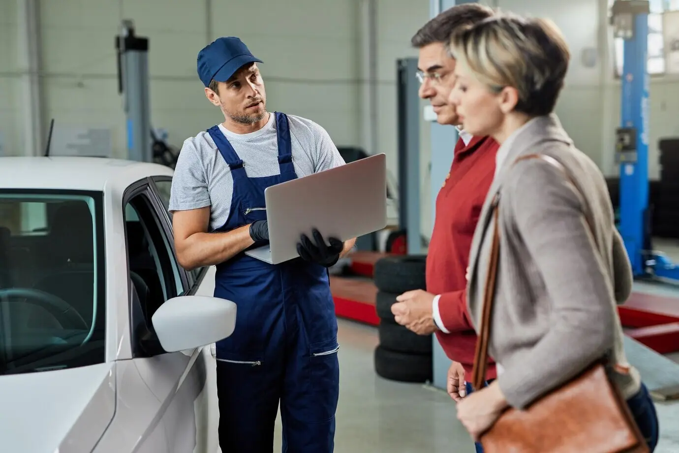 Ein Automechaniker kommuniziert in einer Werkstatt mit seinen Kunden, während er einen Laptop benutzt.
